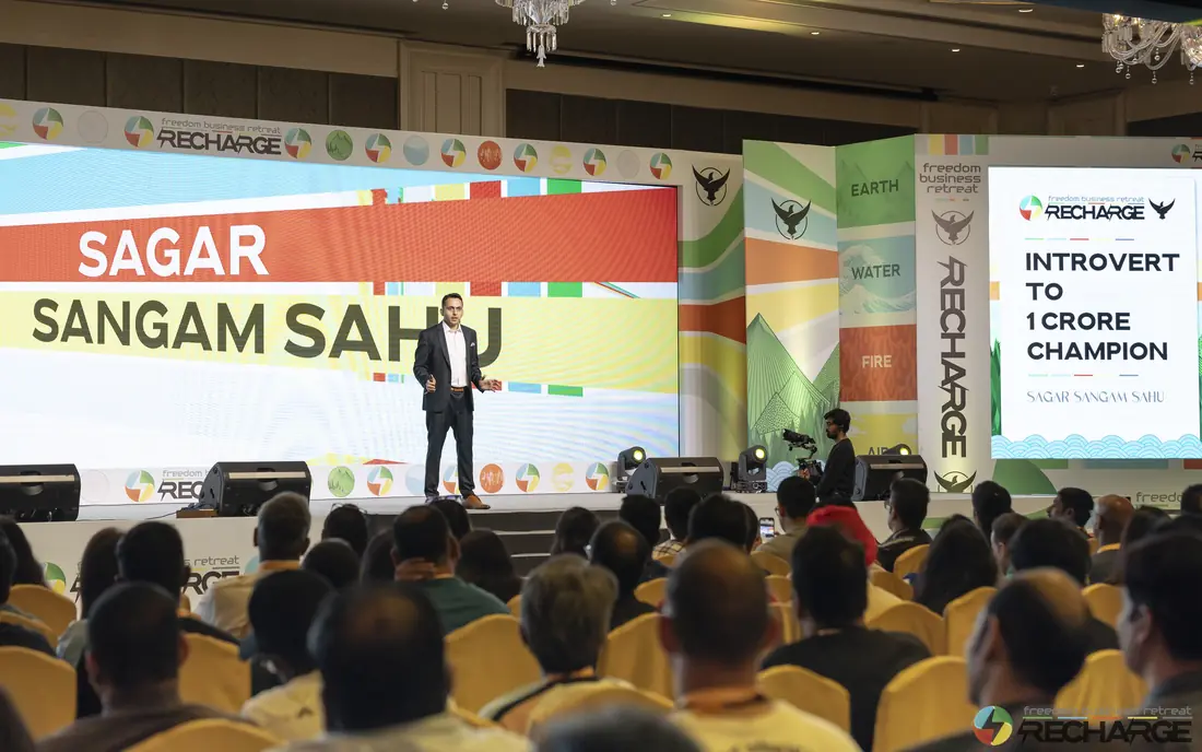 Sagar Sangam Sahu on stage at Recharge, under a banner that reads Introvert to 1 Crore Champion